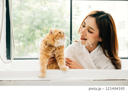 A clean and happy moment in the bathroom, a woman and her Scottish Fold cat enjoy bath time together, a scene of pure owner-pet love. A clean and happy moment in the bathroom, a woman and her Scottish Fold cat enjoy bath time together, a scene of pure owner-pet love. 121494395