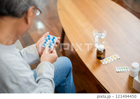 Asian worried senior man with medicine pills to taking on table in the living room, old man buy herbal self cure Rx pill online from pharmacy, home isolation, health care help service 121494450