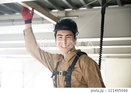 安全帯をつけて笑顔のカメラ目線の作業着の若い男性 安全帯をつけて笑顔のカメラ目線の作業着の若い男性 121495098