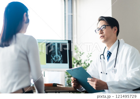 問診行う男性ドクターと腰のあたりを抑える女性患者 問診行う男性ドクターと腰のあたりを抑える女性患者 121495729