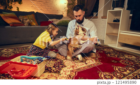 Bearded man and his daughter simulate checkup for their dog during game, using toy medical tools, emphasizing playful learning and pet care. Cozy living room Bearded man and his daughter simulate checkup for their dog during game, using toy medical tools, emphasizing playful learning and pet care. Cozy living room 121495890