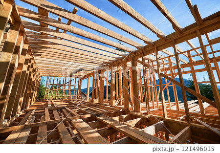 Residential wooden frame building in progress near a forest. Start of new construction of comfortable house. The idea of modern ecological building techniques and contemporary architecture. Residential wooden frame building in progress near a forest. Start of new construction of comfortable house. The idea of modern ecological building techniques and contemporary architecture. 121496015