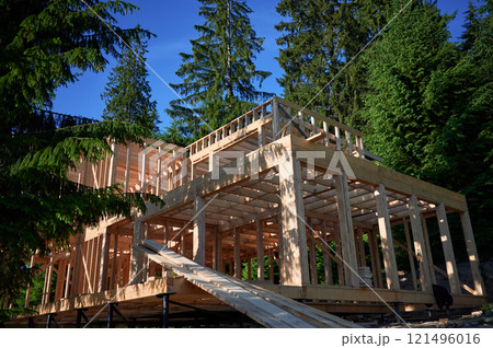 Residential building with wooden frame in process of being built near a forest. Beginning of new construction of comfortable cottage. Idea of ecological construction, contemporary architectural design 121496016