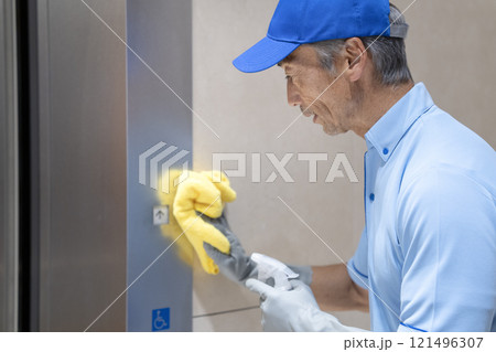 ビル清掃イメージ　エレベーターのボタンを拭くシニアの男性清掃スタッフ 121496307