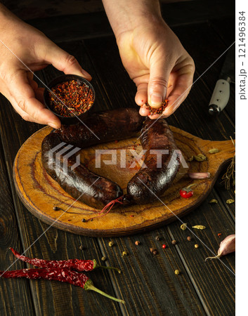 Expert hands prepare a delicious recipe while showcasing plump sausages and vibrant spices on a rustic wooden board. The atmosphere is rich with culinary tradition and flavor Expert hands prepare a delicious recipe while showcasing plump sausages and vibrant spices on a rustic wooden board. The atmosphere is rich with culinary tradition and flavor 121496384
