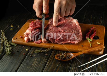 Skillful hands expertly slice fresh meat on a wooden cutting board in a rustic kitchen 121496385