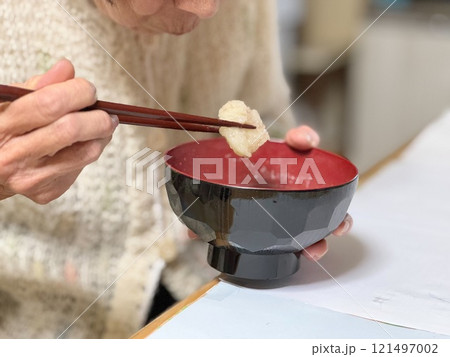 じゃがいも団子を箸で持ち上げる高齢女性 121497002