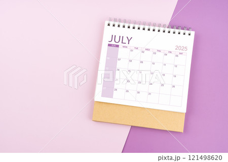 July 2025 desk calendar on pink and purple background. 121498620