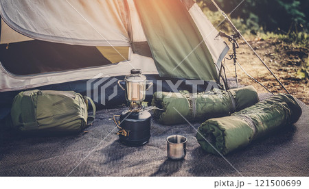 A camping tent with a black stove and a silver cup on the ground A camping tent with a black stove and a silver cup on the ground 121500699