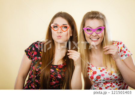 Two happy women holding fake eyeglasses on stick Two happy women holding fake eyeglasses on stick 121501403