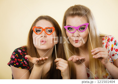 Two happy women holding fake eyeglasses on stick 121501404