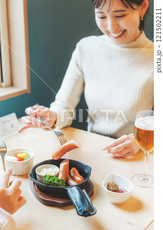 クラフトビールのおつまみにソーセージを食べる女性二人 121502211