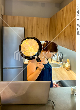 A young girl in the kitchen near an electric stove holds a frying pan in her hands and tries to figure out the equipment 121502659