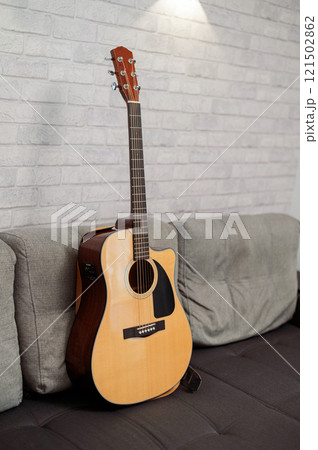 Beautiful six-string acoustic guitar, wood body, on sofa in studio 121502862