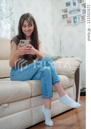 Happy pleasant millennial woman relaxing on comfortable couch, holding smartphone in hands. Smiling young lady chatting in social networks, watching funny videos Happy pleasant millennial woman relaxing on comfortable couch, holding smartphone in hands. Smiling young lady chatting in social networks, watching funny videos 121502872