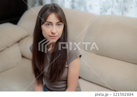 peace woman sitting comfortably on a gray couch at home, smiling and relaxing in soft natural light during the afternoon 121502884
