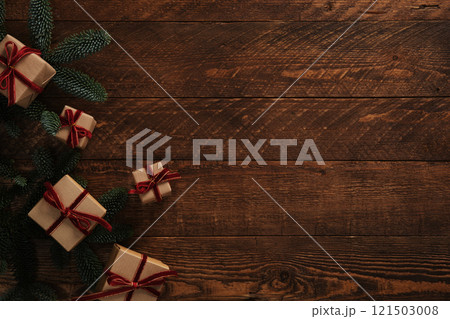 Christmas gifts in brown kraft paper with red velvet ribbons and sprigs of evergreen fir trees on a brown wooden background. Space for your text. Christmas gifts in brown kraft paper with red velvet ribbons and sprigs of evergreen fir trees on a brown wooden background. Space for your text. 121503008