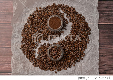 Fresh aromatic grain and ground coffee in transparent glasses on craft paper, wooden table. Composition in the form of yin yang 121504651