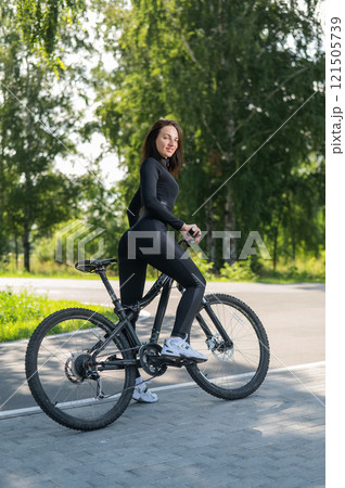 Rear view of Caucasian woman riding bike in park. Vertical photo.  121505739