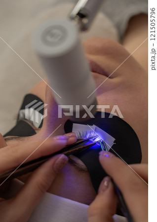 A woman undergoing eyelash extension procedure using an ultraviolet lamp. 121505796