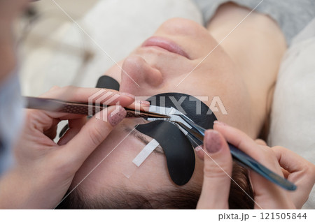 A woman undergoing eyelash extension procedure using an ultraviolet lamp. 121505844