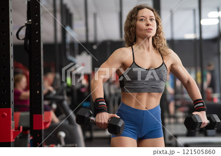 Muscular Caucasian forty year old woman doing exercises with dumbbells in the gym. Muscular Caucasian forty year old woman doing exercises with dumbbells in the gym. 121505860