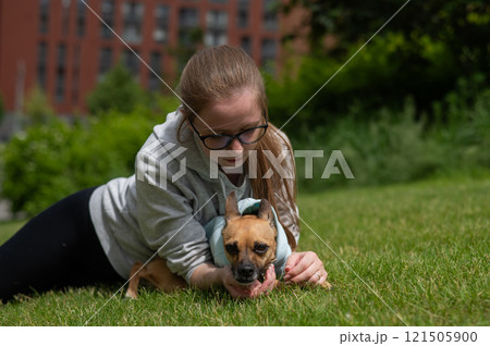 Young Caucasian woman lying on the lawn while walking with a small dog.  121505900