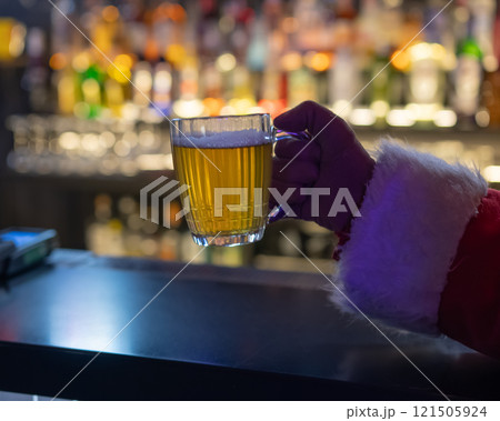 Santa Claus drinking beer at a bar. Close-up of a hand holding a mug of beer.  121505924