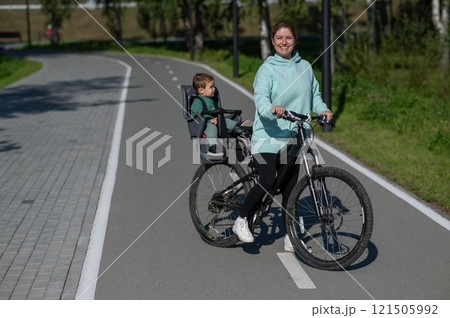Caucasian woman riding a bicycle with her toddler son sitting behind her in a child seat.  121505992