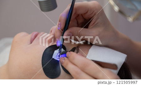 A woman undergoing eyelash extension procedure using an ultraviolet lamp. 121505997