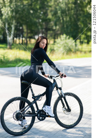 Rear view of Caucasian woman riding bike in park. Vertical photo.  121506044