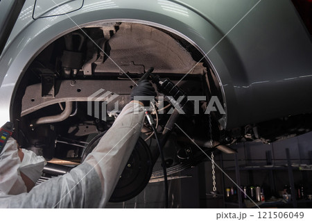 An auto mechanic applies anti-corrosion mastic to the underbody of a car. An auto mechanic applies anti-corrosion mastic to the underbody of a car. 121506049