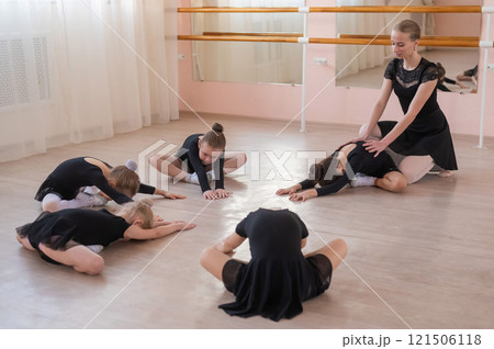Caucasian woman and five little girls sit in a circle and do stretching at a ballet school. Caucasian woman and five little girls sit in a circle and do stretching at a ballet school. 121506118