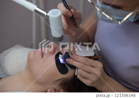 A woman undergoing eyelash extension procedure using an ultraviolet lamp. 121506148