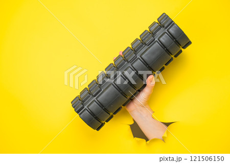 Female hand sticking out with MFR roller from yellow paper background. 121506150