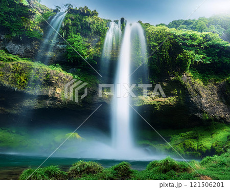 Majestic waterfall cascading down a lush green cliff into a river below, surrounded by vibrant foliage and a clear blue sky 121506201