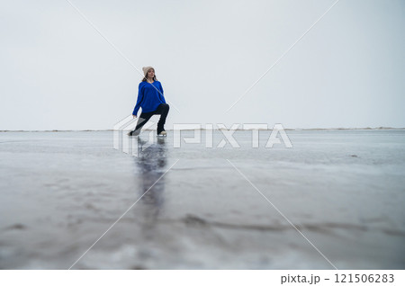 Caucasian woman in a blue sweater is skating on a frozen lake. The figure skater performs the program. 121506283
