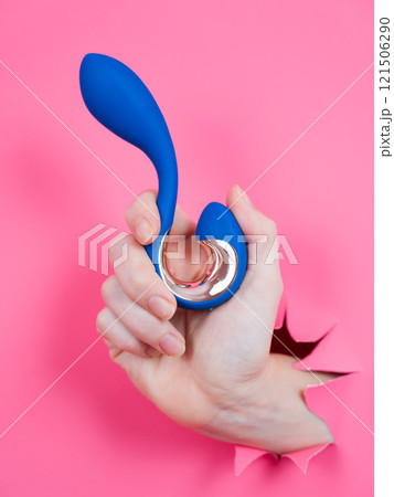 Hand with blue vibrator sticking out through pink paper background. Vertical photo.  121506290