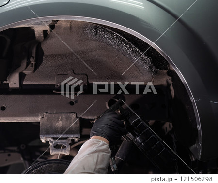 An auto mechanic applies anti-corrosion mastic to the underbody of a car. 121506298