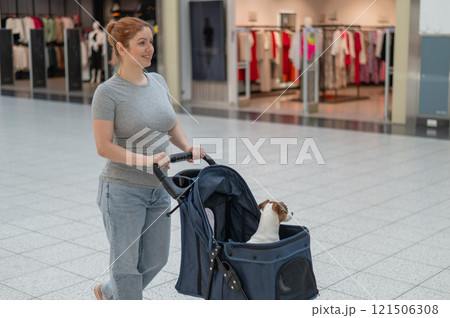 A Caucasian woman is shopping with her Jack Russell Terrier dog in a stroller in a shopping mall. A Caucasian woman is shopping with her Jack Russell Terrier dog in a stroller in a shopping mall. 121506308