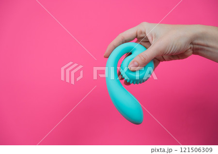 Woman holding blue curved sex toy on pink background. Copy space. Woman holding blue curved sex toy on pink background. Copy space. 121506309