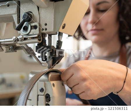 A woman tanner sews a leather belt on a sewing machine.  121506311