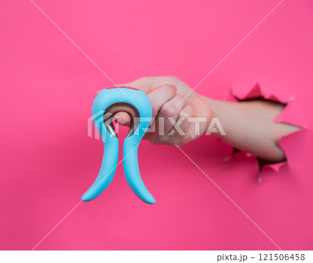 Female hand sticking out of pink paper background with blue curved vibrator sex toy.  121506458