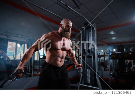 Bald Caucasian bodybuilder training chest using cable crossover in gym.  121506462