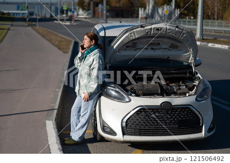 Sad Caucasian woman calling on phone while standing near car with open hood.  121506492