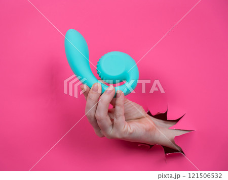 Hand with blue vibrator sticking out through pink paper background. Copy space. Hand with blue vibrator sticking out through pink paper background. Copy space. 121506532