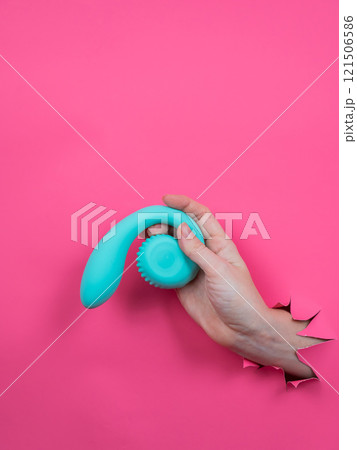 Hand with blue vibrator sticking out through pink paper background. Vertical photo.  121506586
