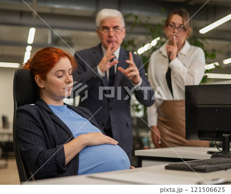 Elderly Caucasian man and woman giggling behind their sleeping pregnant colleague in the office.  121506625