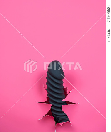 Black ribbed dildo sticking out of hole on pink background. Vertical video.  121506686