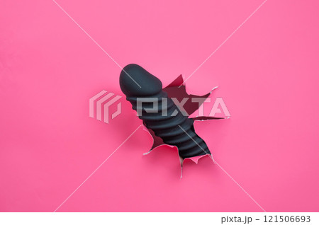Black ribbed dildo sticking out of hole on pink background. Black ribbed dildo sticking out of hole on pink background. 121506693